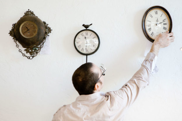 Man photographed from behind adjusting one of 3 clocks on the wall