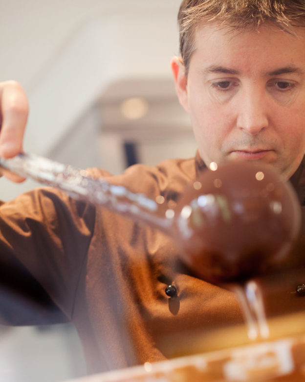 Photograph of a chocolate maker pouring liquid chocolate from a ladle