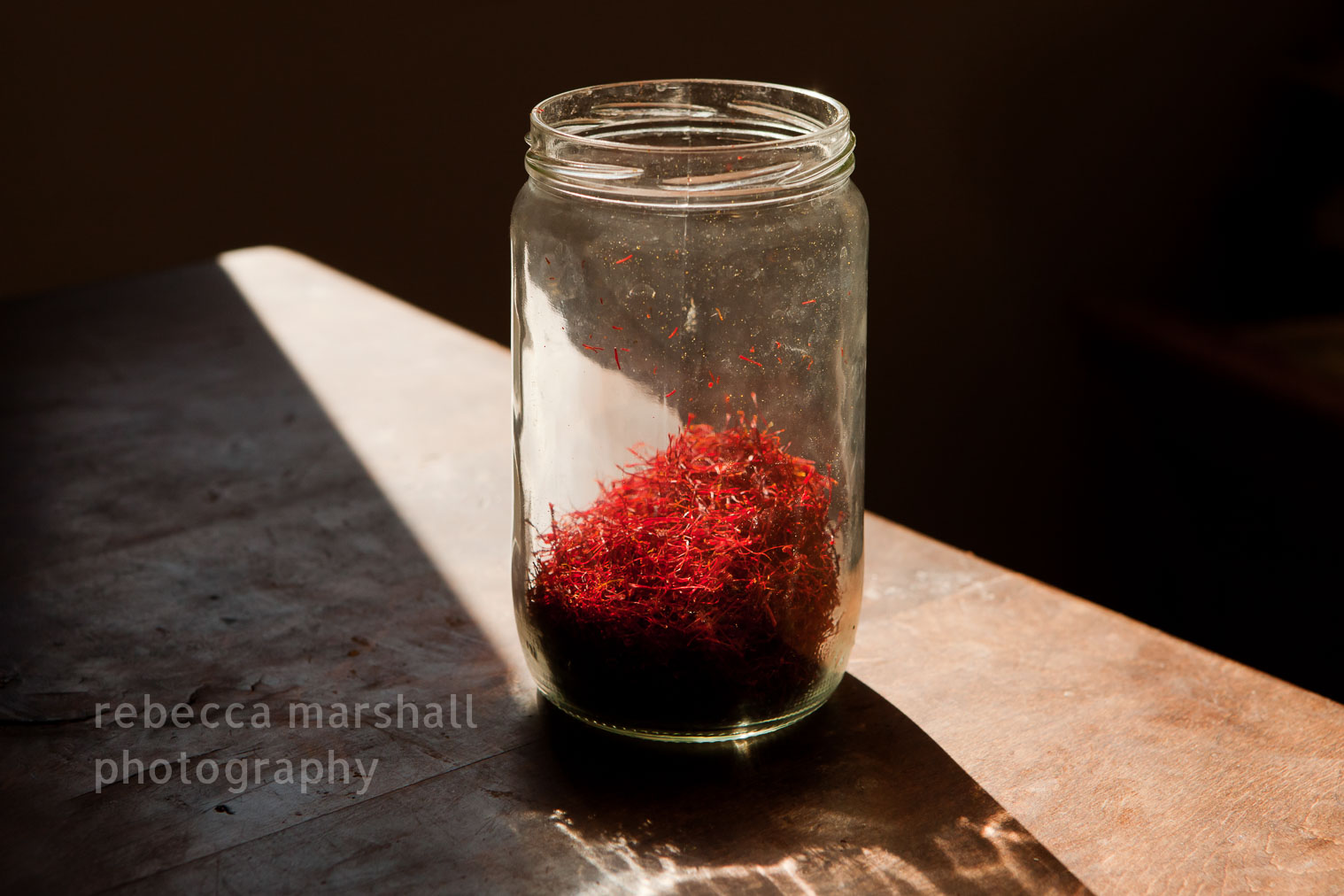 Photograph of a jar one-third full of dried saffron, red in the sunlight