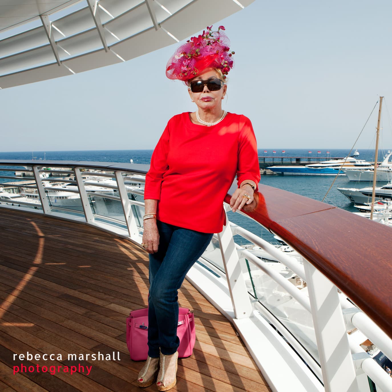 Portrait of Baroness von Brandstetter, posing in bright red, on the rails of the terrace of Monaco Yacht Club