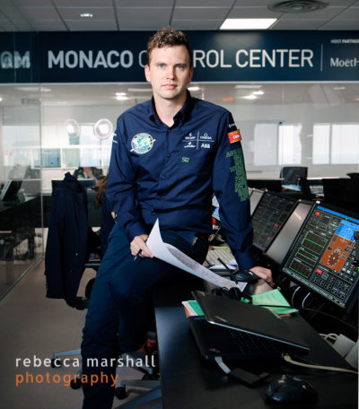 Portrait of engineer Michael Anger sitting on a desk beside a line of computer screens in the Mission Control Centre