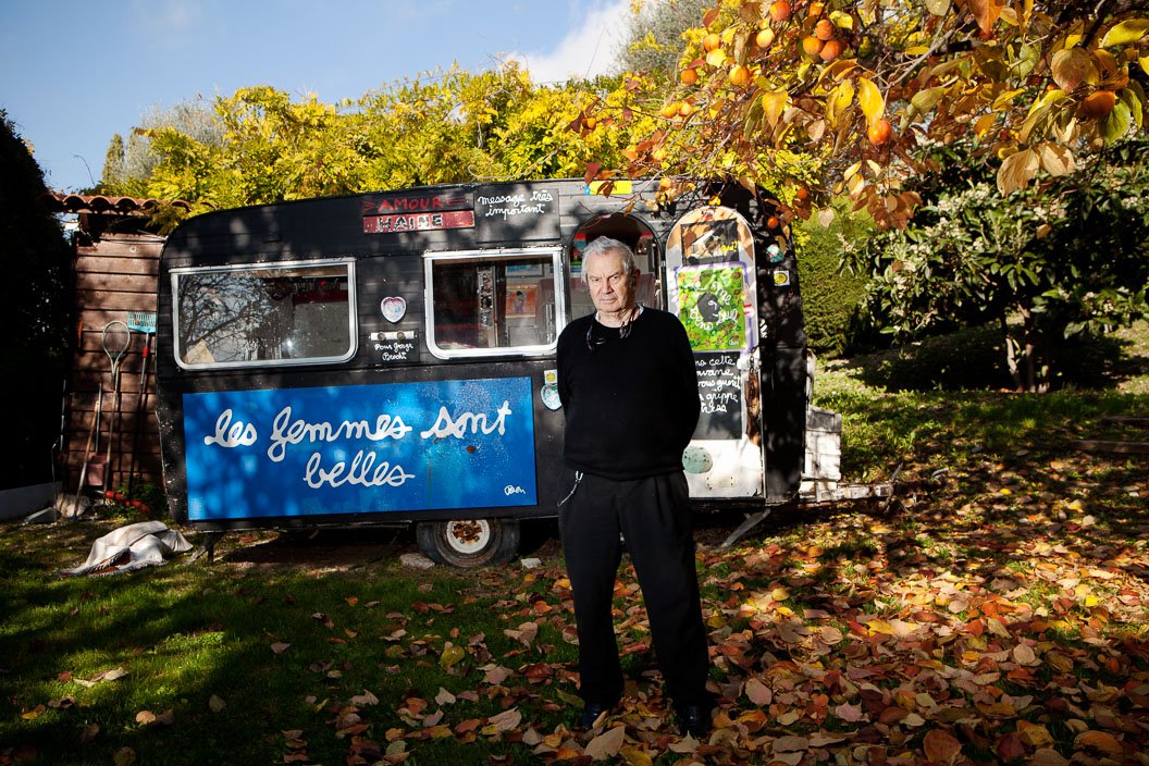 Environmental portrait of artist Ben standing in front of a painted caravan in his garden