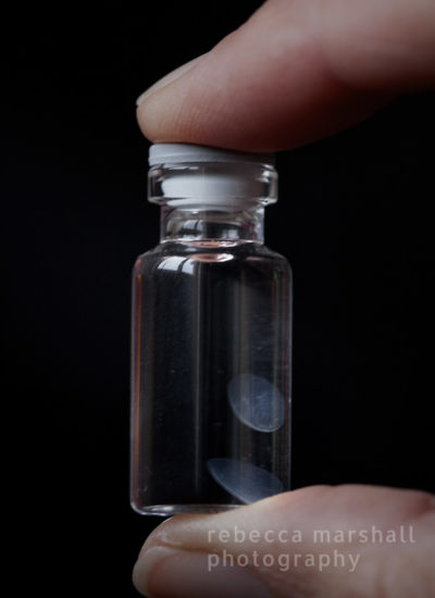 Close-up photograph of a small har held between finger and thumb, containing 2 floating lenticules on a black background