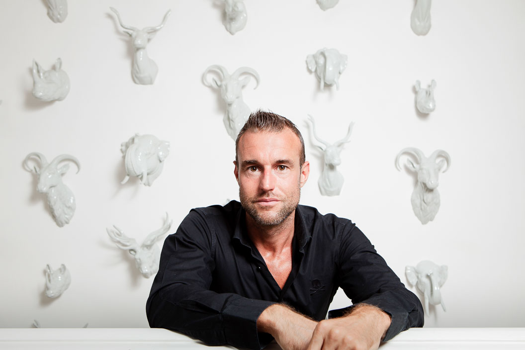 Portrait of a man in a black shirt in front of a white wall of animal head statues
