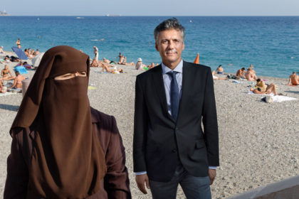 Photograph of a woman wearing a burqa and man in a suit on a beach in summer