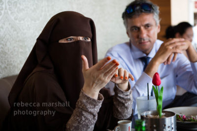 Photograph of woman in niqab talking to an interviewer with man in suit next to her