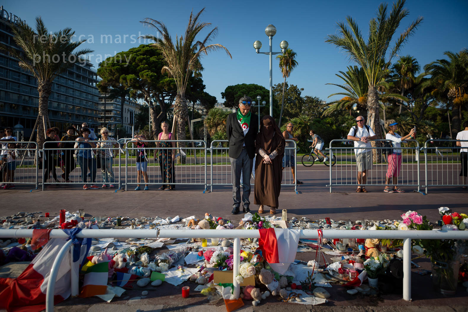 Man and woman in burqa pay their respects in front of pile of flowers