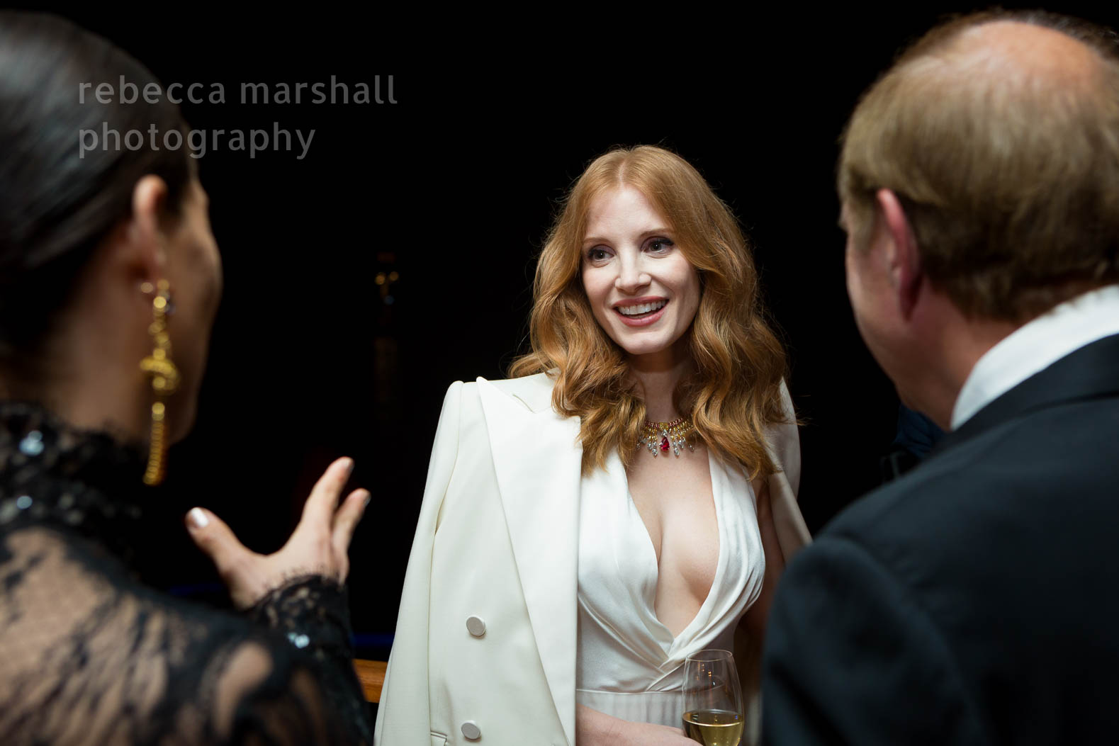 Photograph of Jessica Chastain, in a white dress, talking at a party