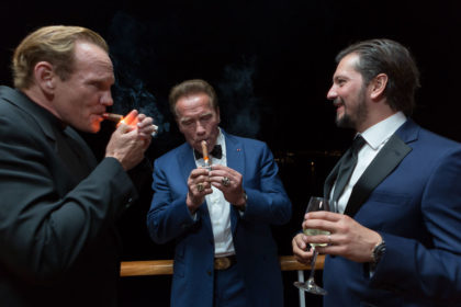Arnold Schwarzenegger lights a cigar with two friends at a party