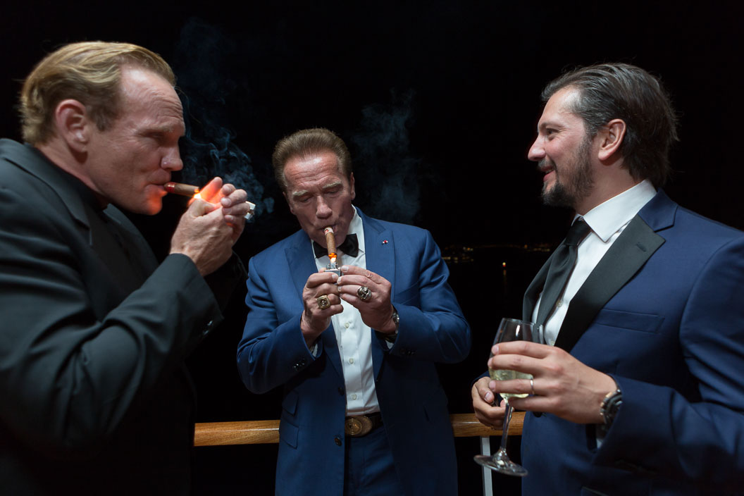 Arnold Schwarzenegger lights a cigar with two friends at a party