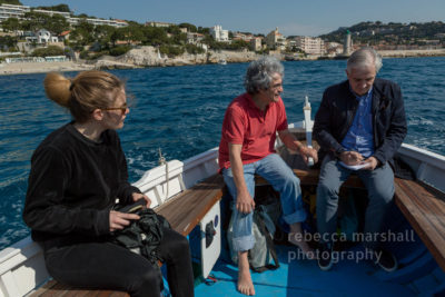 Photograph of 3 people in the back of a fishing boat: Carlo Rovelli is interviewed by a journalist; a girl watches them.