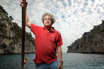 Portrait of a man in a red t-shirt standing up in a small boat in a cove