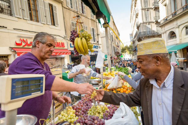 Man wearing a traditional African hat buying fruit from a market stall