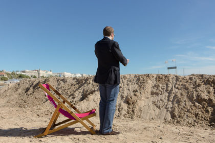 Man in suit on beach next to pink deckchair on telephone