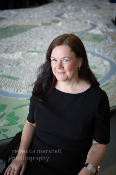 Portrait of woman in black, seated, beside large model of the city of London