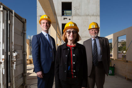 Horizontal portrait of 2 men and a woman in hard hats in the middle of a building site