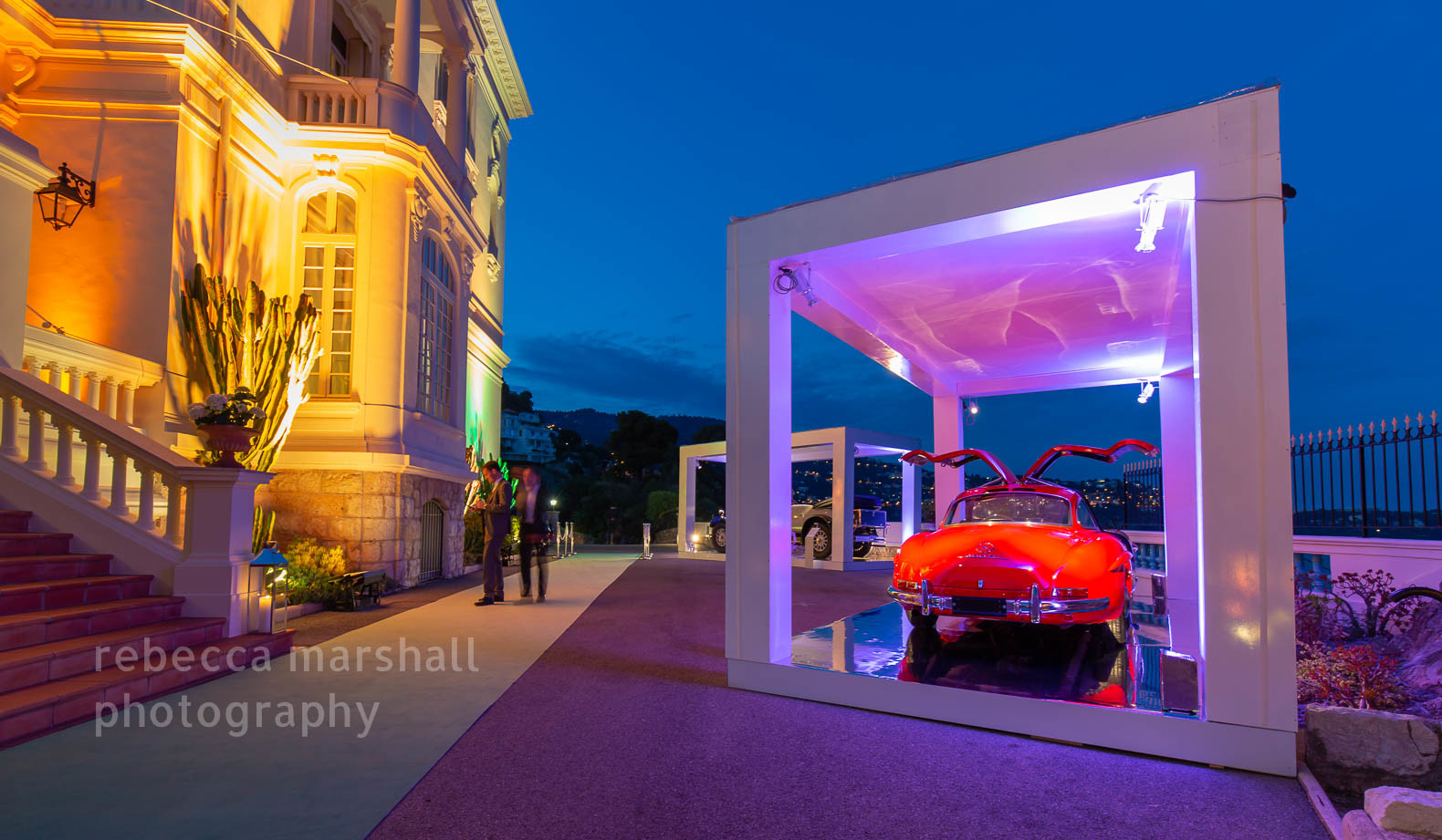 Dusk photograph showing red vintage Mercedes sports car on display in front of a villa