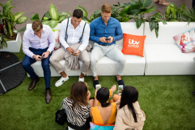 Photo from overhead of 3 men and 3 women sitting on white couches