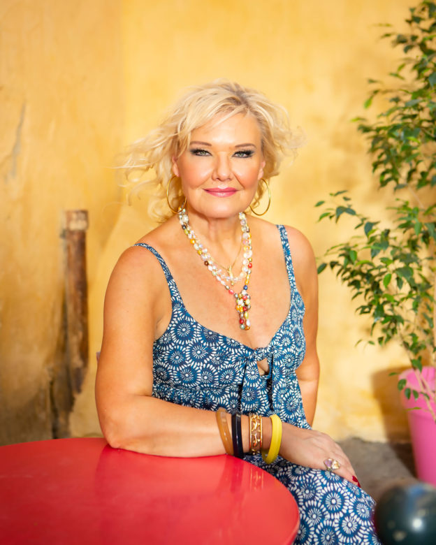 Portrait of Karita Mattilia seated at a red table in front of a yellow wall