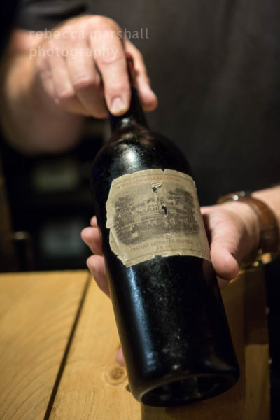 Close-up photograph of man's hands holding a very old bottle of vintage wine.