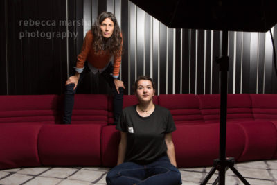 Photograph of indoor, single umbrella photographic lighting set-up for a double portrait and two women posing for light tests