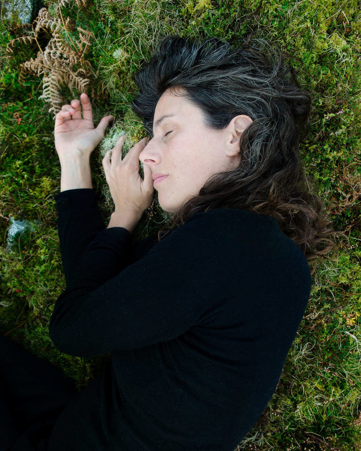 Self portrait of Rebecca Marshall with eyes closed lying on her side in moss