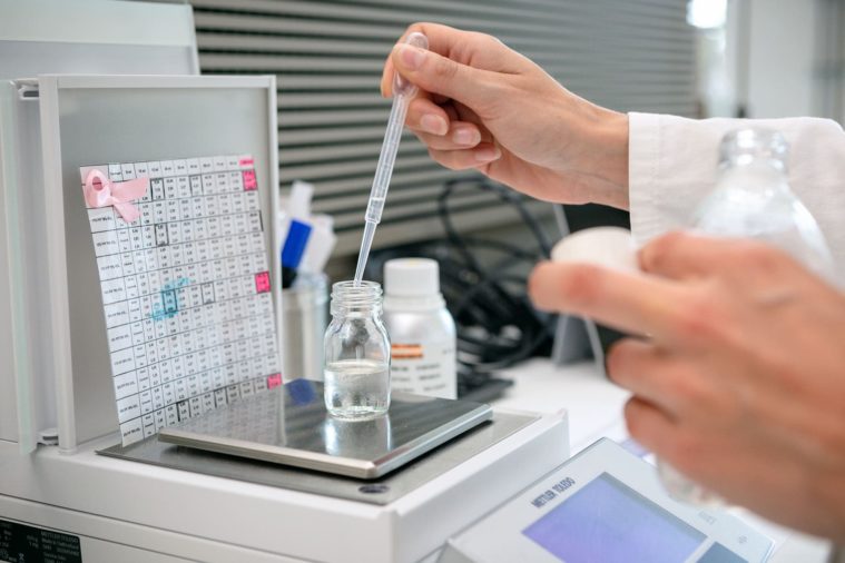 Close-up photo of hands squeezing liquid from a pipette into a small bottle in a laboratory