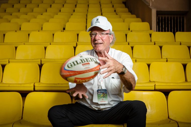 Man in cap sitting on yellow chairs in an empty stadium catches a rugby ball