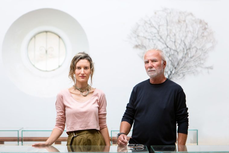 A woman and a man pose for the camera in a white room