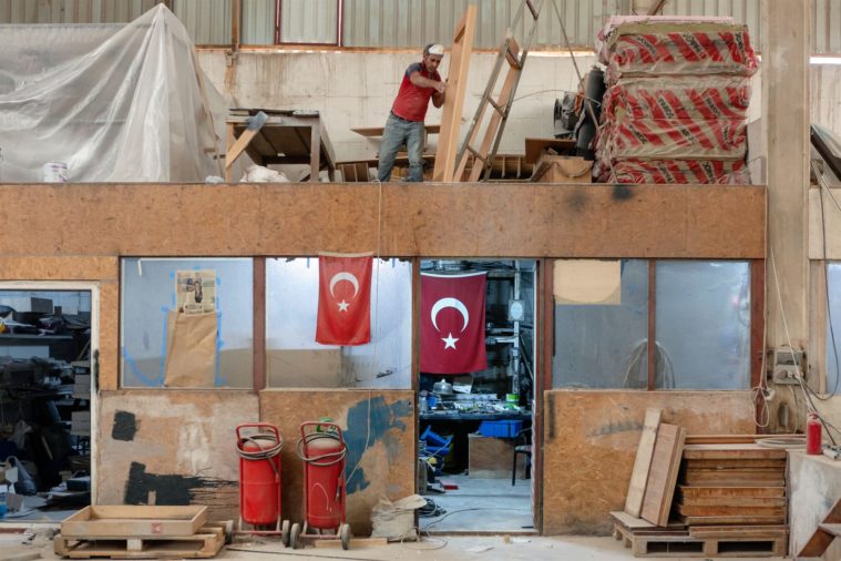 Photograph of an office inside a boatyard with the Turkish flag hanging up and a workman moving a piece of wood