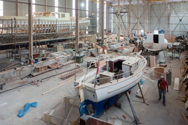 Wide view of the interior of a boatyard hangar with 3 boats visibly under construction