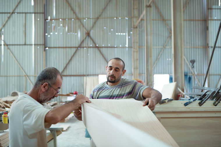 2 craftsmen holding and measuring a piece of wood