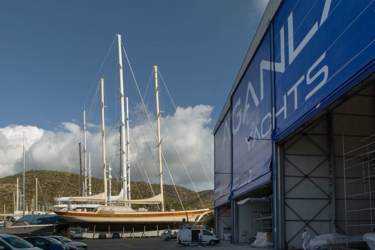 Exterior photo of a boatyard hangar entrance and a yacht in the sunshine