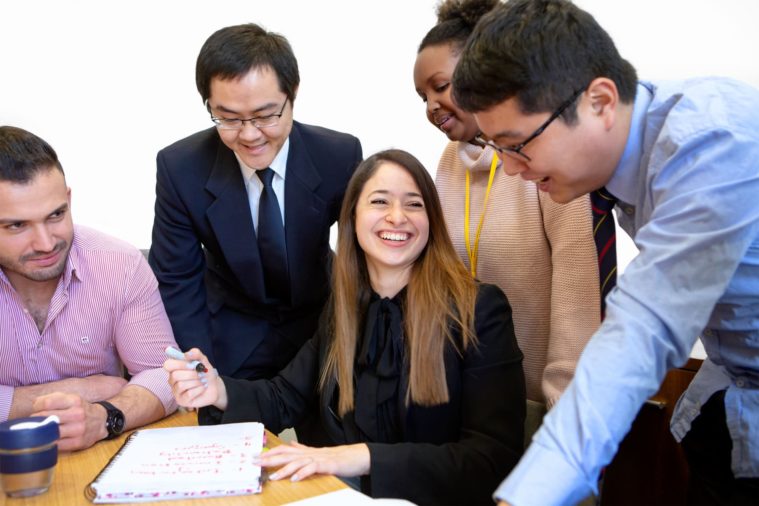 5 students laugh together as they work at a table