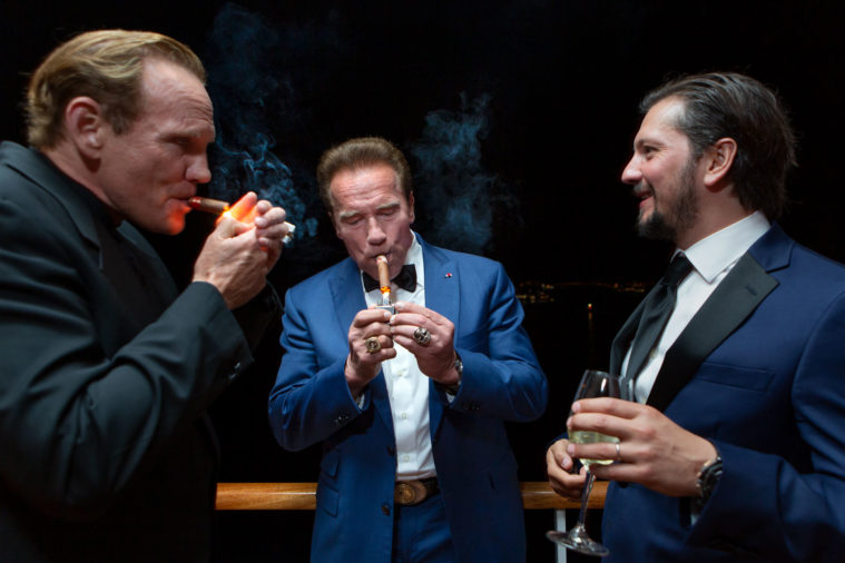 3 men in eveningwear light cigars on a balcony at night