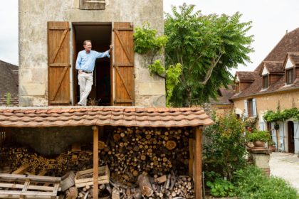 Man stands in open window of a first floor pigeon house and looks out over the woodshed below