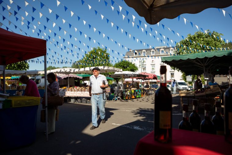 A man wearing a beret walks through a French market under a blue sky