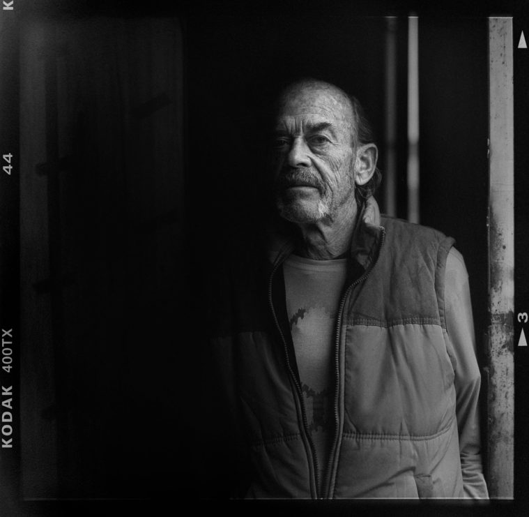 Black and white medium format photograph of a low key portrait of a man (with Kodak film rebate visible)