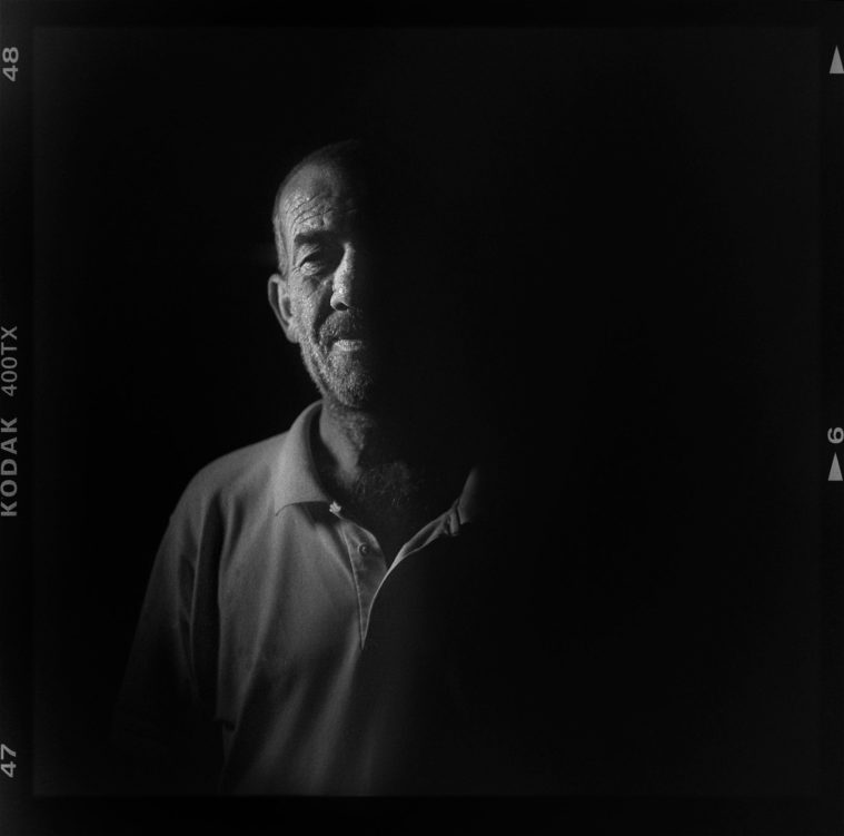 Black and white medium format photograph of a low key portrait of a side-lit man (with Kodak film rebate visible)