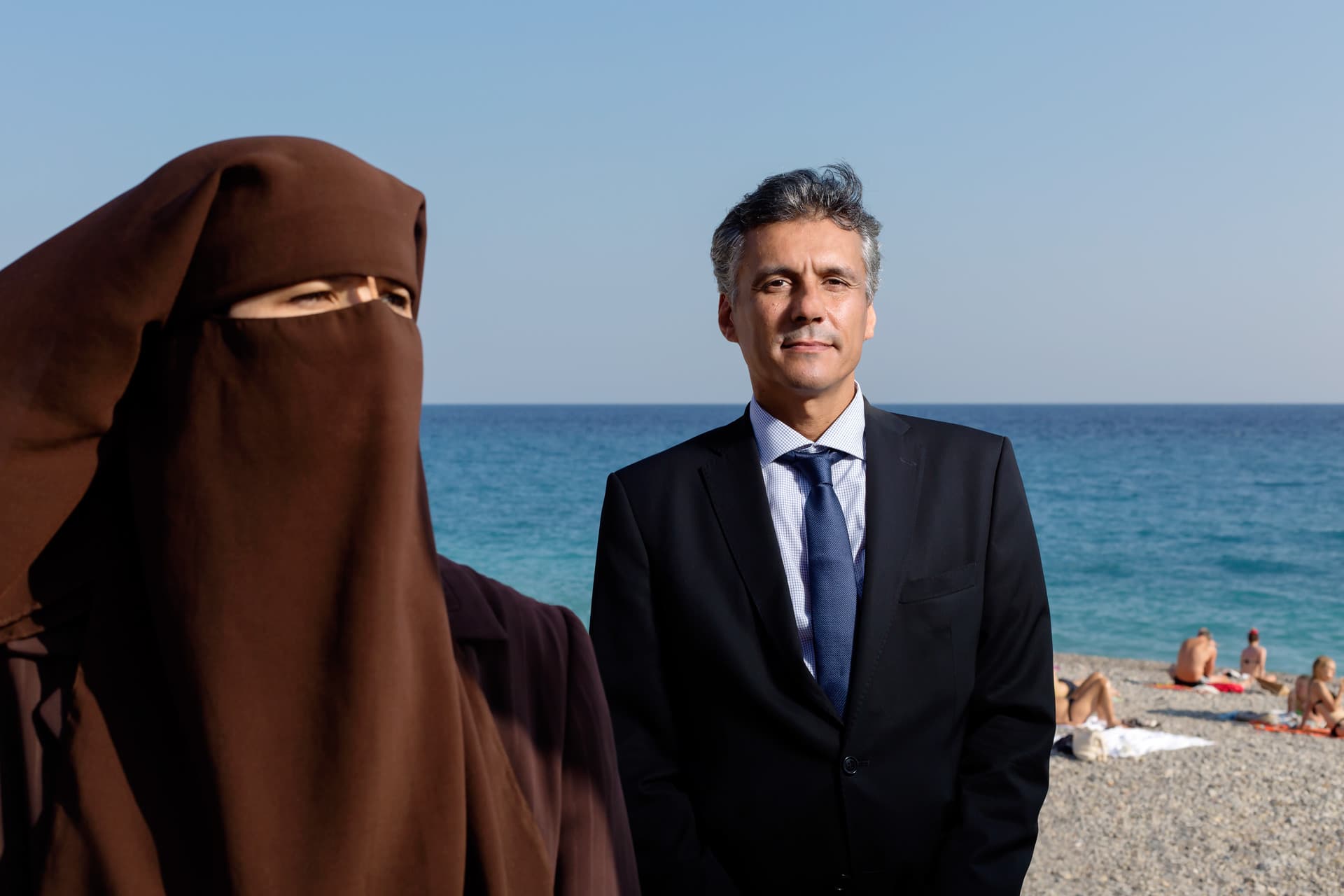 Woman wearing a niqab and man in a suit on a beach in the sunshine