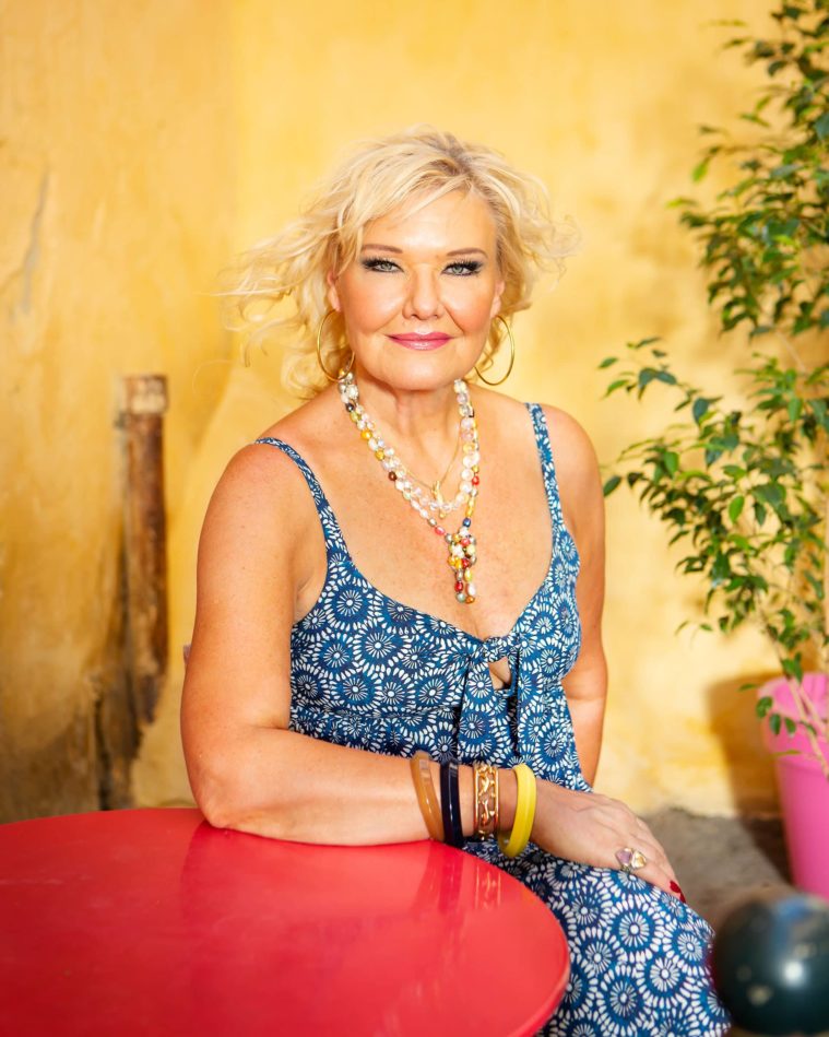 Blonde woman sits at a red table in front of a yellow wall