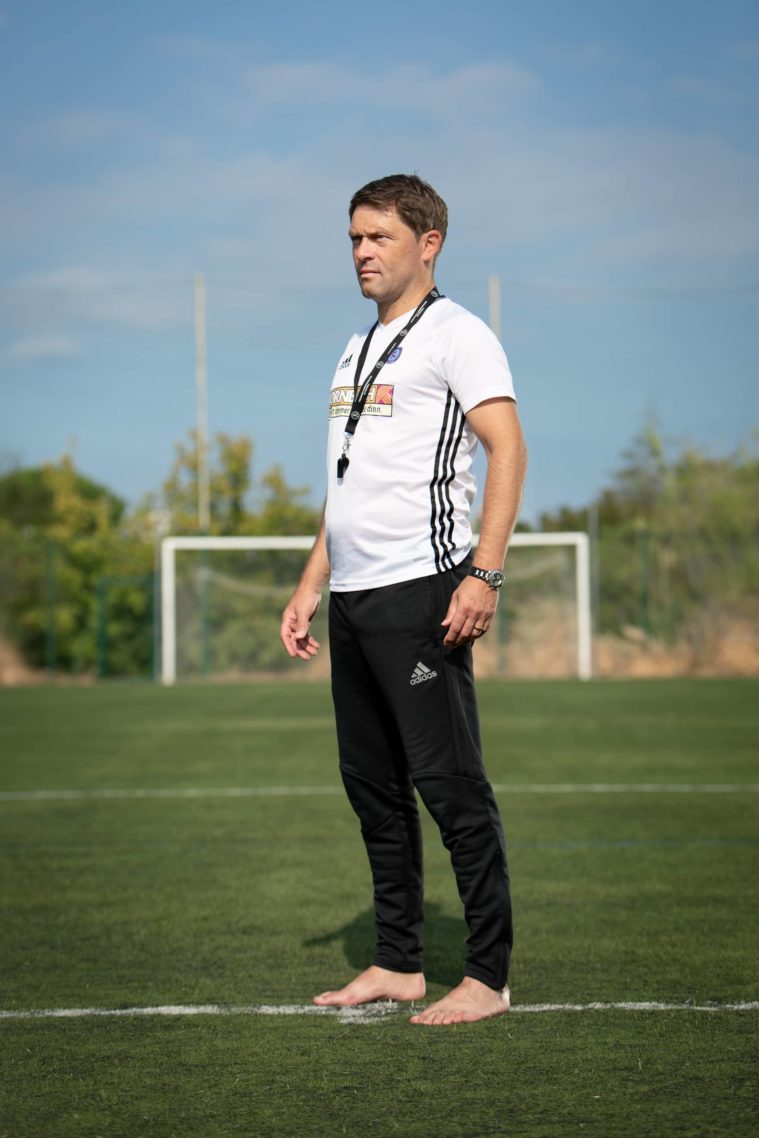 Man stands barefoot on a football pitch