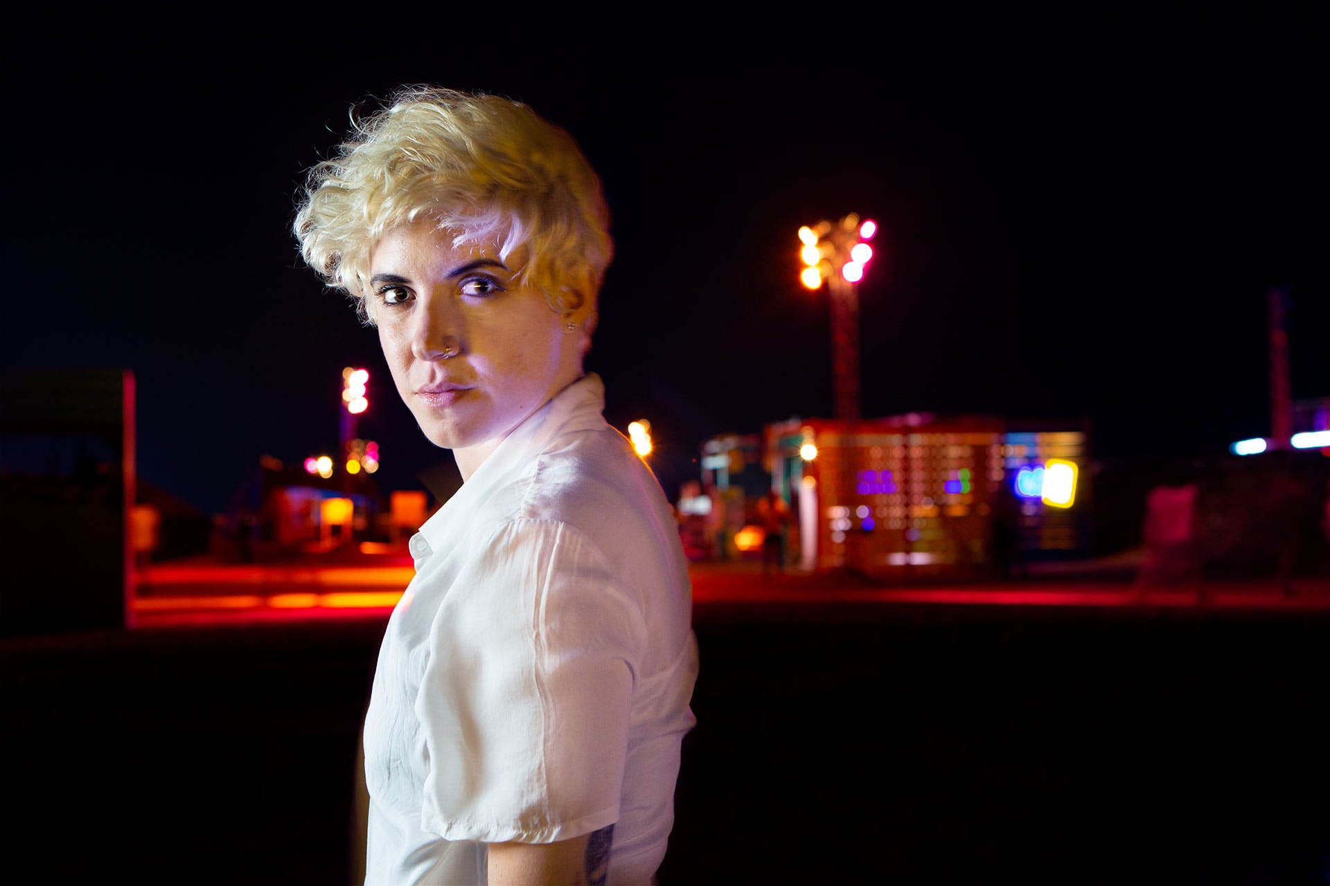 Portrait of woman in white shirt at night with coloured lights in background