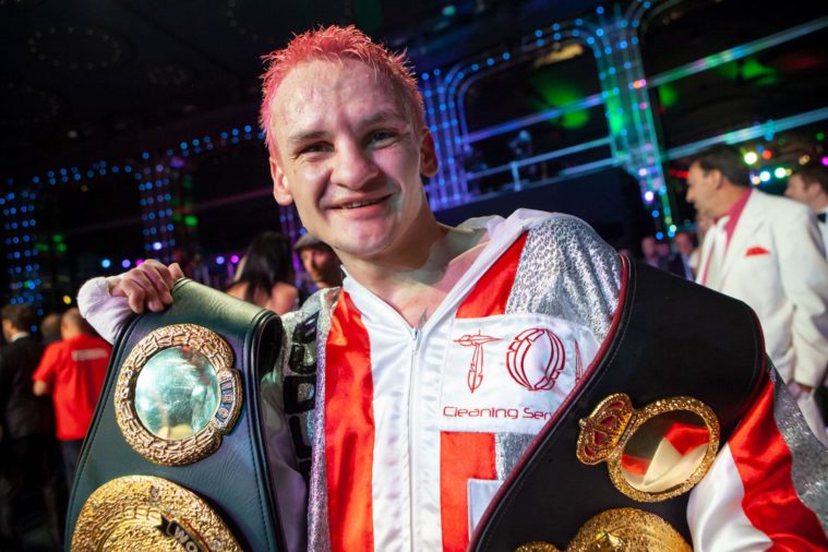 Boxer smiles at camera with champion&#039;s belt around his shoulders