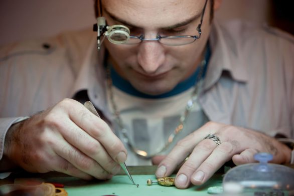 Close-up photograph of a man wearing magnifying glasses repairing a watch