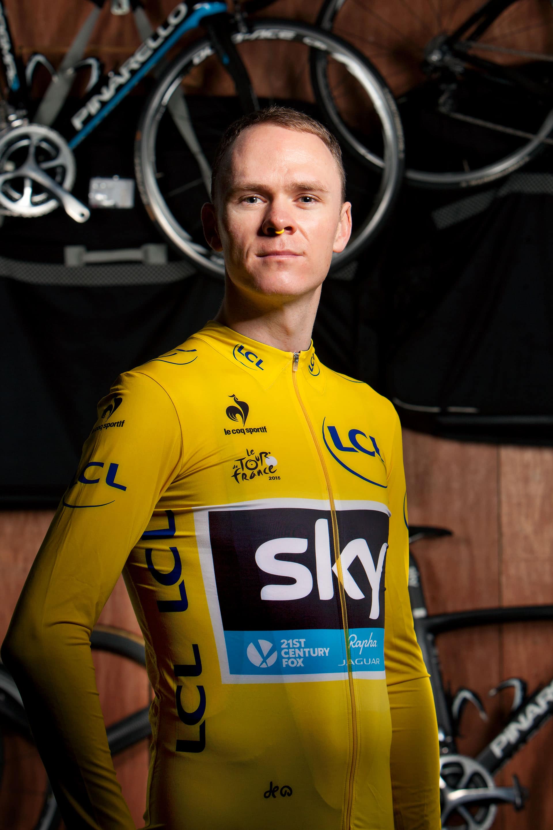 Cyclist in yellow jersey stands in front of bicycles on the wall