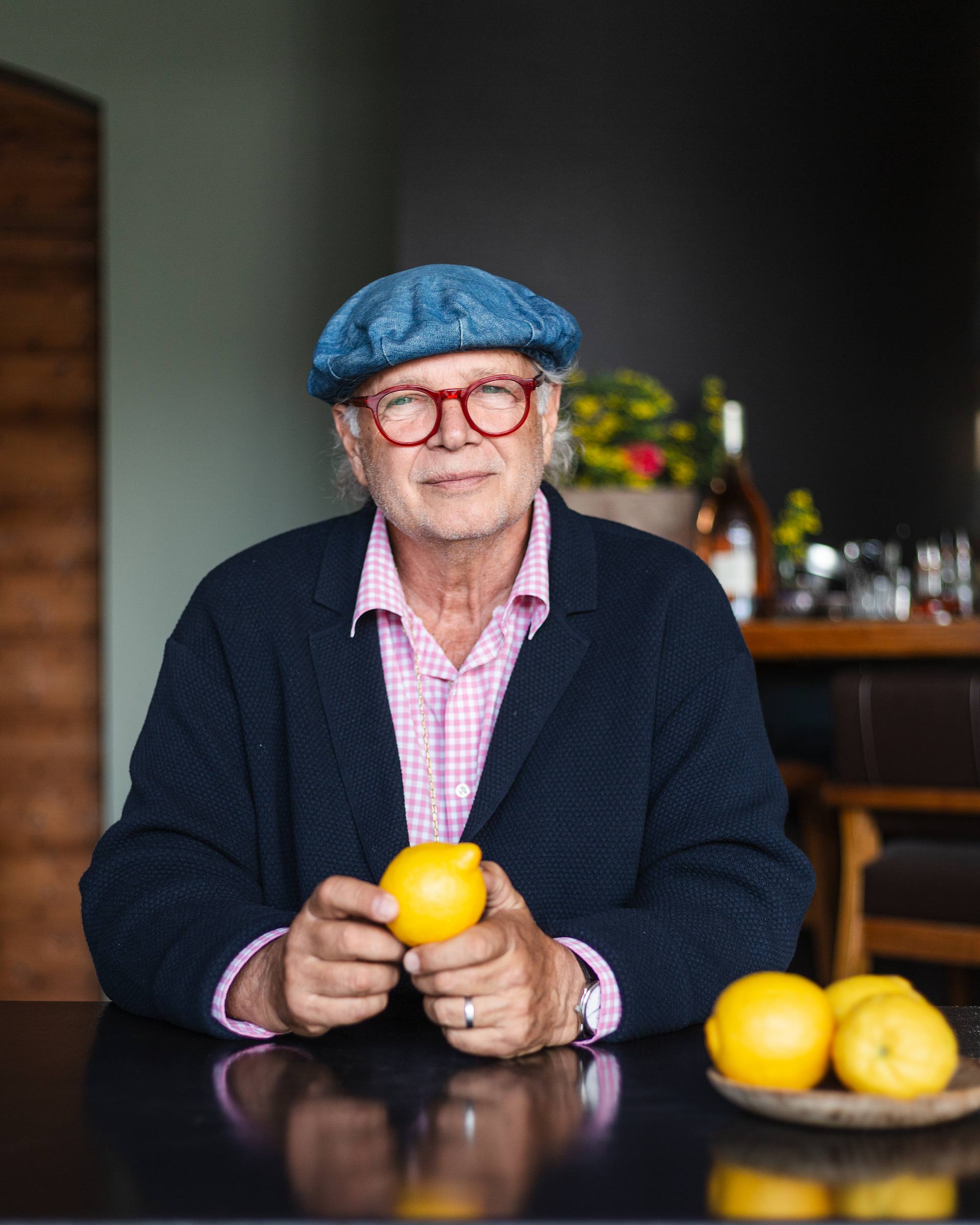 Portrait of a man in a blue cap and red glasses, sitting at a table with lemons