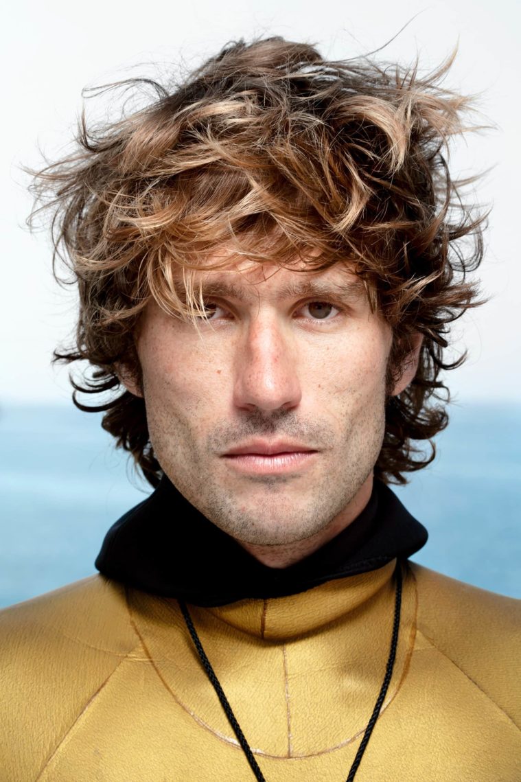 Close-up portrait of man in a gold wetsuit with the sea in the background