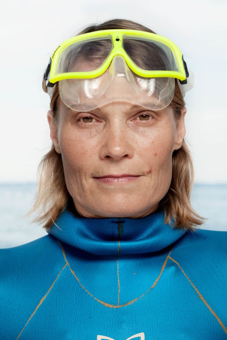 Close-up portrait of woman in a wetsuit with a scuba mask on her head and the sea in the background
