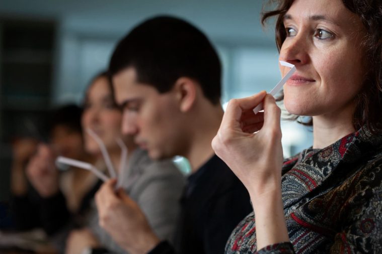 Woman smelling perfume tester strip, other people smelling strips out of focus in background